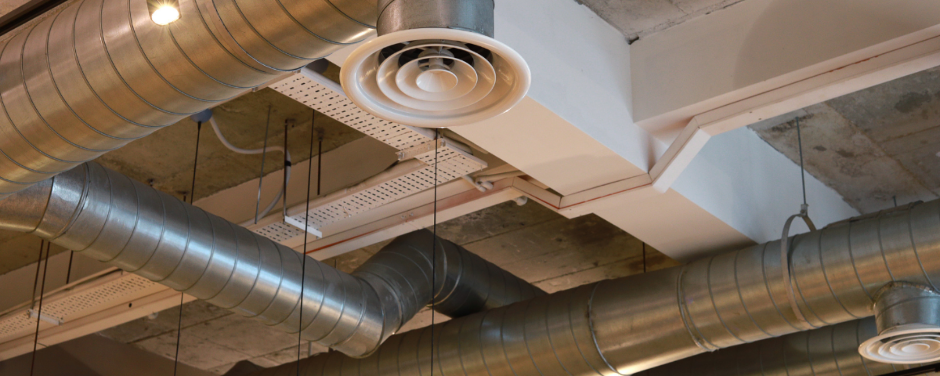 Large metal tubes are mounted onto a warehouse ceiling and are used for air conditioning.