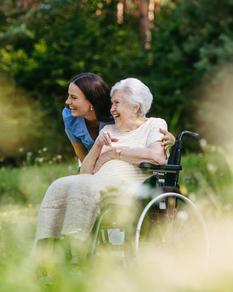 An elderly lady in a wheelchair is hugged by a woman.