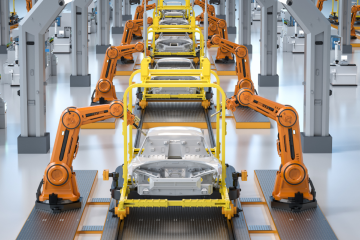 A car production plant. Each car body has two robotic arms working on it.