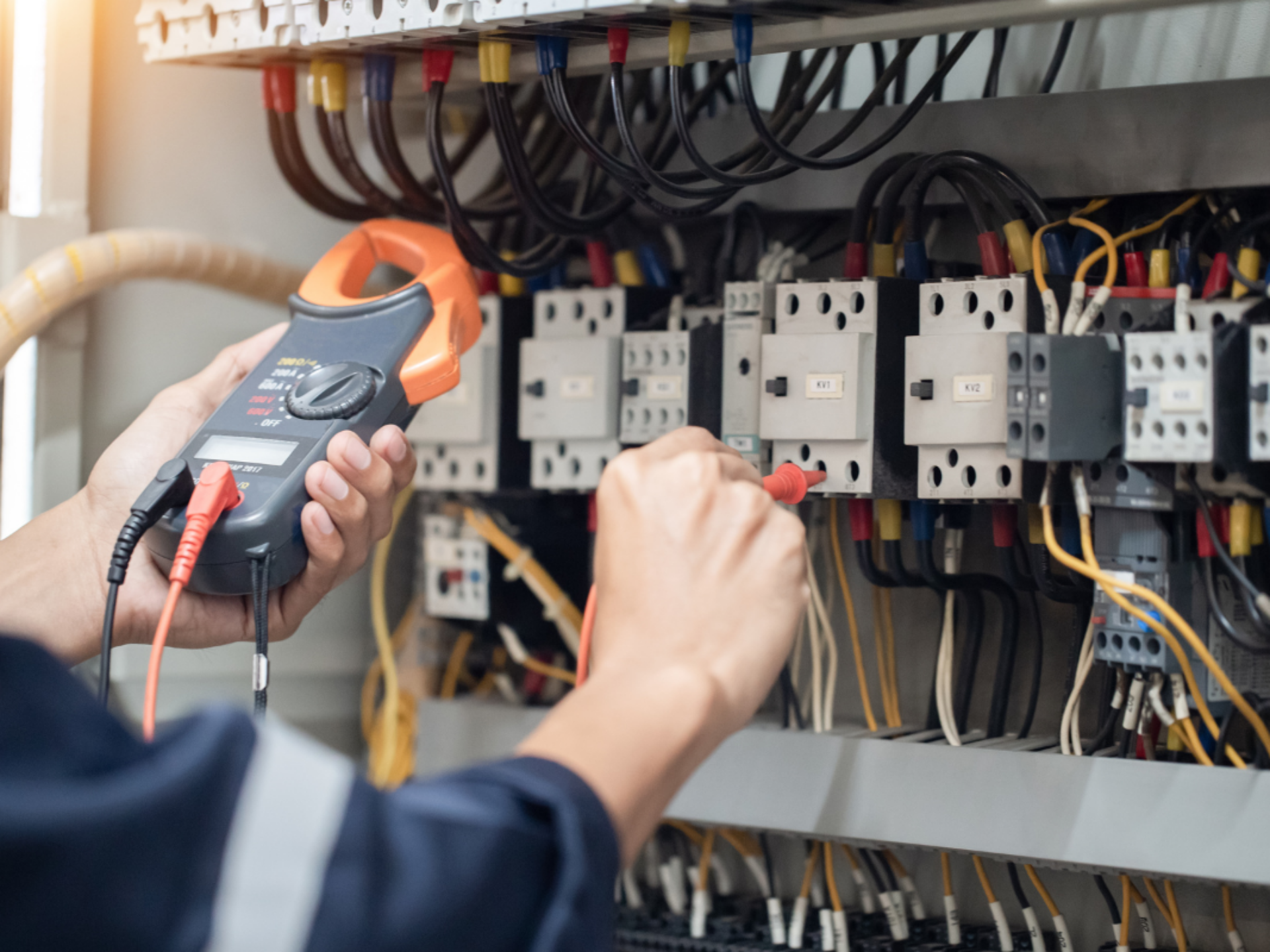 An electrician is performing tests on an electrical board, using a measuring device attached to a probe to take readings.