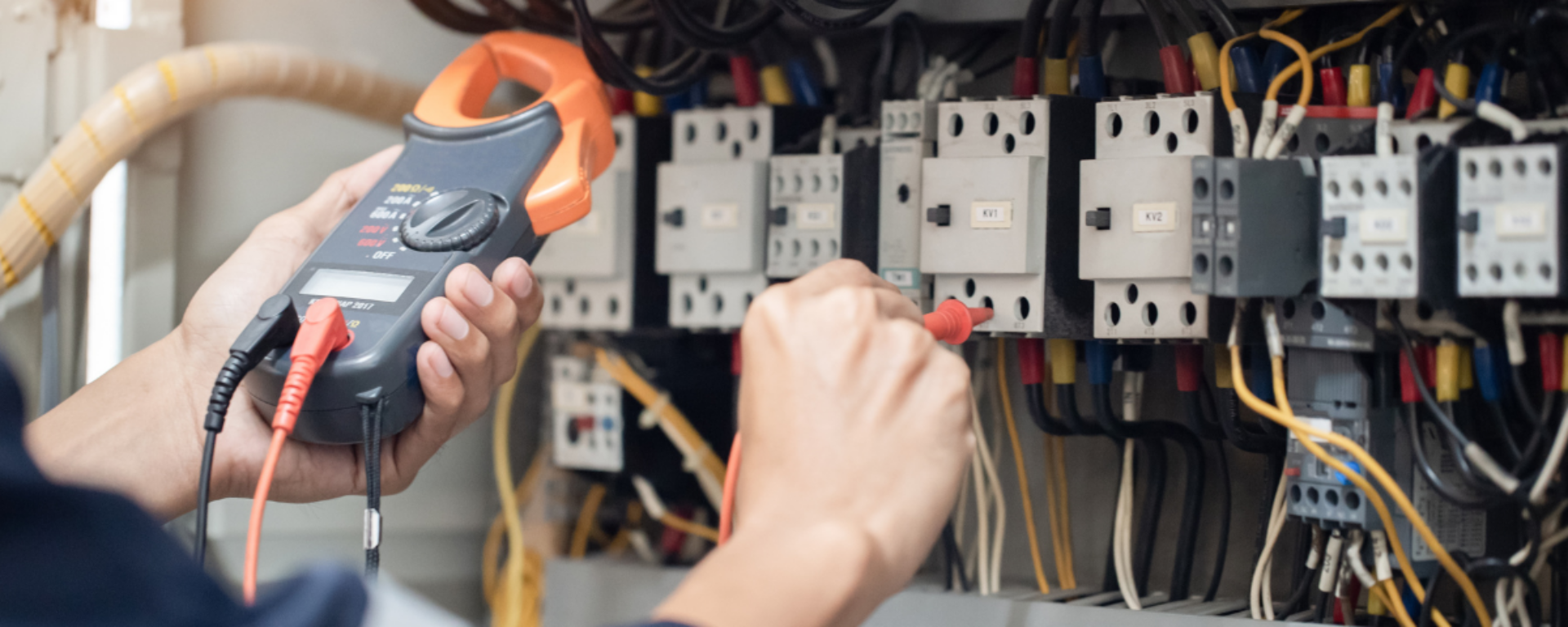 An electrician is performing tests on an electrical board, using a measuring device attached to a probe to take readings.