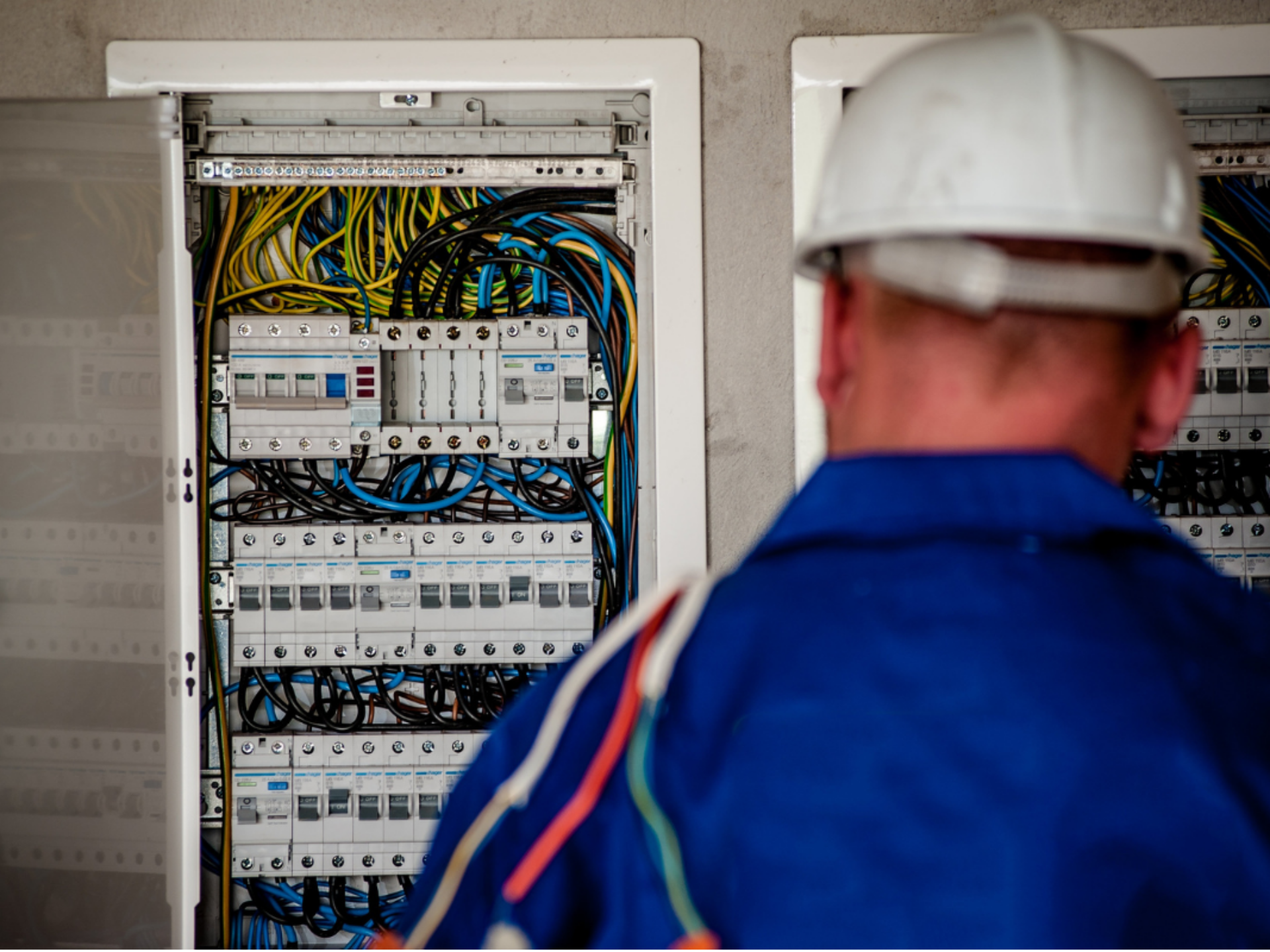 An open electrical cupboard is seen over the shoulder of a electrician.