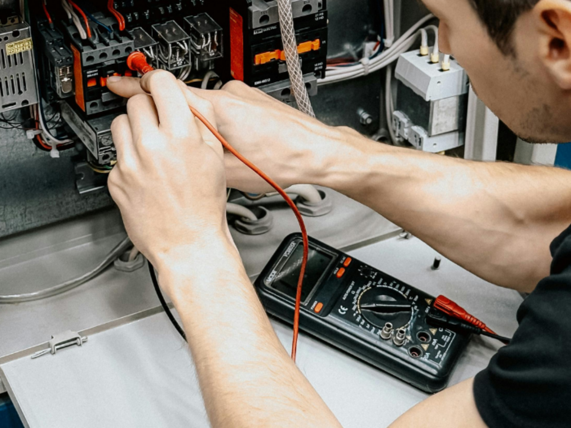 An electrician is performing tests on an electrical board, using a measuring device attached to a probe to take readings.