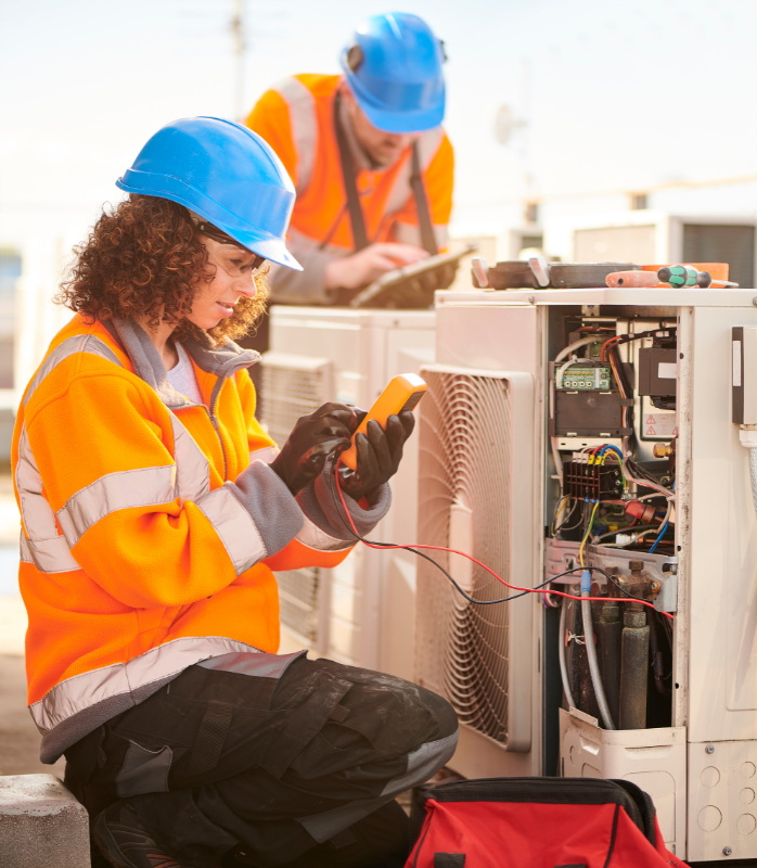 A technician has removed the external air cooler shell and is performing tests using an electronic device and two probes.
